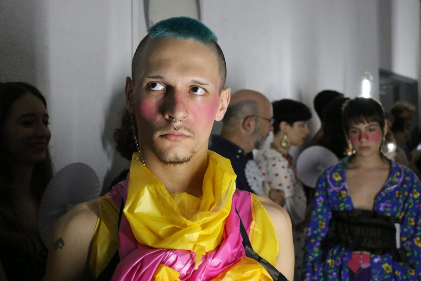 Figure in bright pink avant-garde outfit in a white gallery corridor